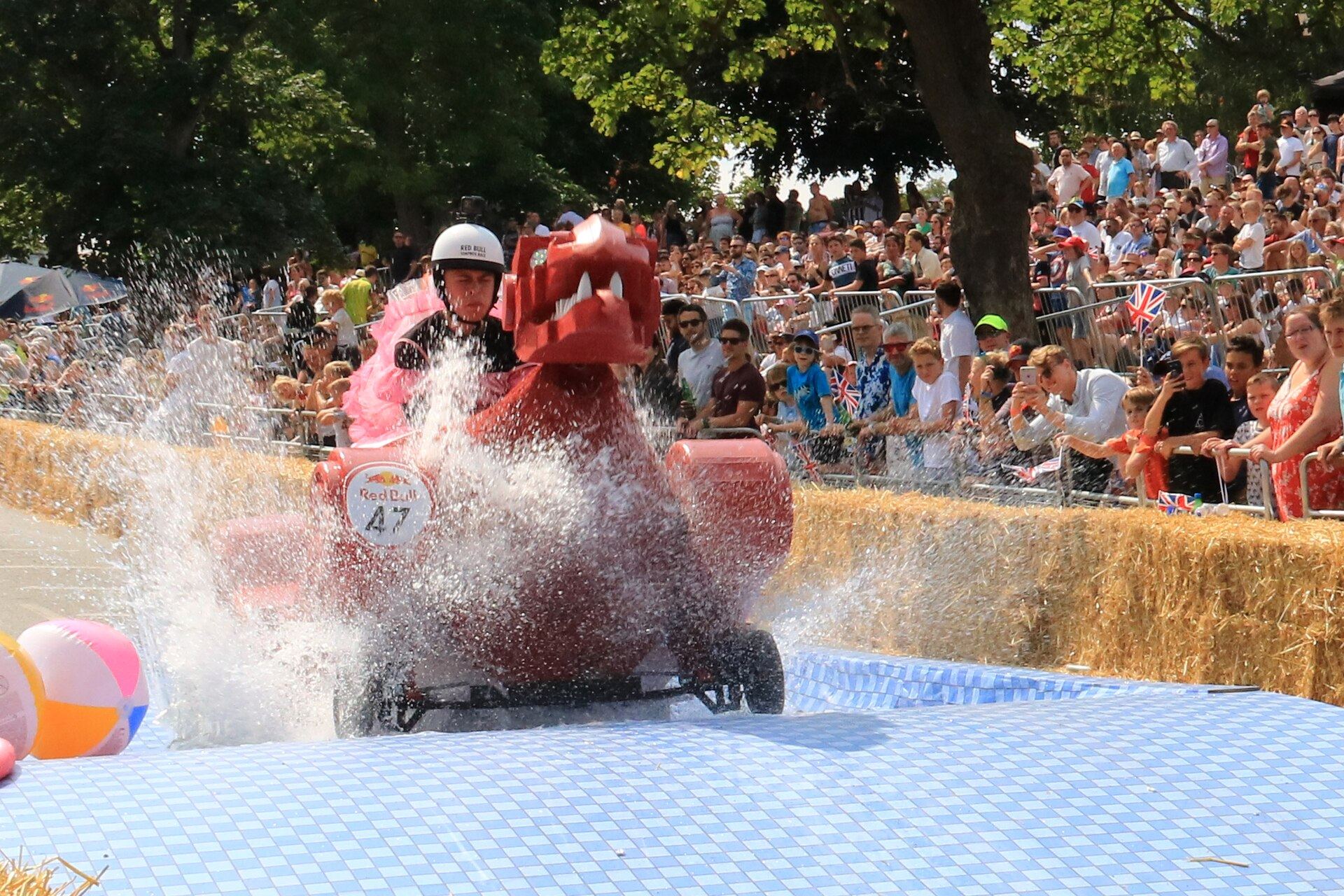 A soapbox racer splashing through a water trap in front of packed crowds at the Red Bull Soapbox Race